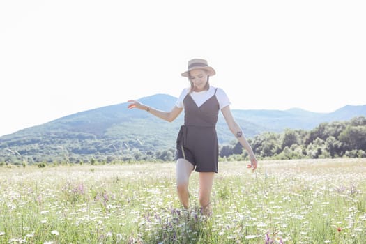 woman in a straw hat walks in a field with daisies flowers in nature