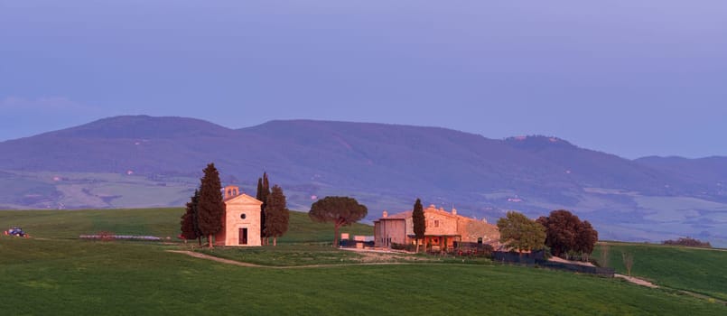 House surrounded by cypress trees among the misty morning sun-drenched hills of the Val d'Orcia valley at sunrise in San Quirico d'Orcia, Tuscany, Italy