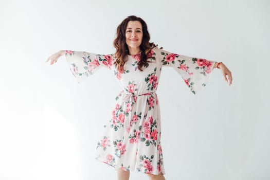 a woman in floral dress stands against a white wall on a white background