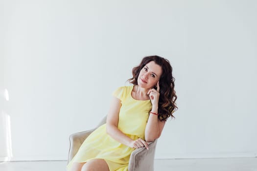 brunette woman in a yellow dress sits in a chair in a bright room