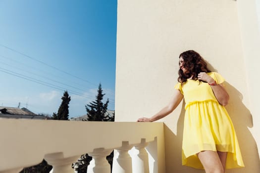 brunette woman in a yellow dress stands on the balcony of the room