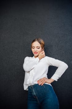 beautiful woman in a white blouse stands against a dark wall