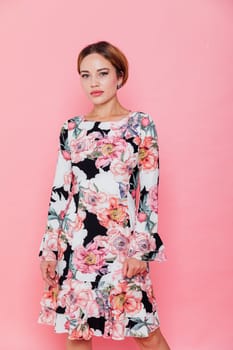 woman in a floral dress stands against a pink wall