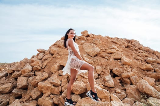woman in white clothes stands by a sandy mountain of stones
