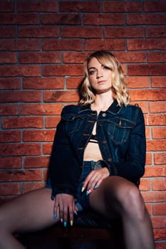 woman in black clothes poses against a brick wall in the shadows