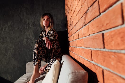 a blonde woman sitting on couch in a room against a red brick wall