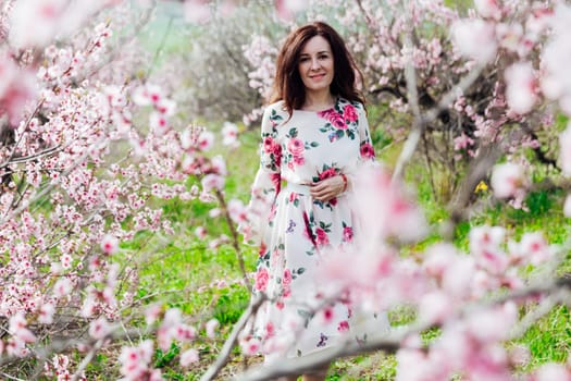 brunette in beautiful dress in pink flowers in a blooming garden walk in spring