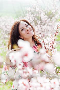 portrait of beautiful brunette woman in pink flowers on the street in a blooming garden