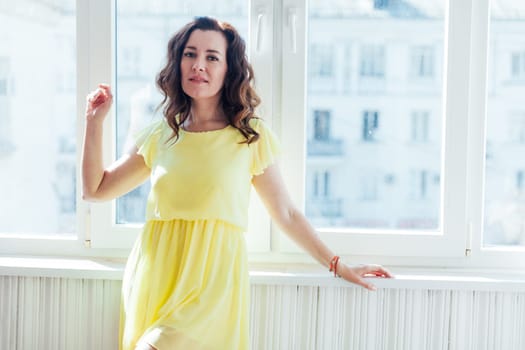 brunette woman standing by a window in a bright room