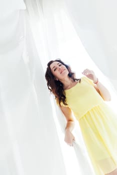 woman in a yellow dress stands in white fabrics in the room