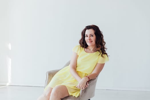 a woman in yellow dress sits in a chair in a bright room