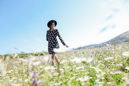 woman in a polka dot dress and hat stands in a daisy field in nature