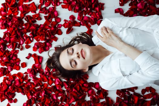 a woman lies on the floor with her eyes closed in red rose petals