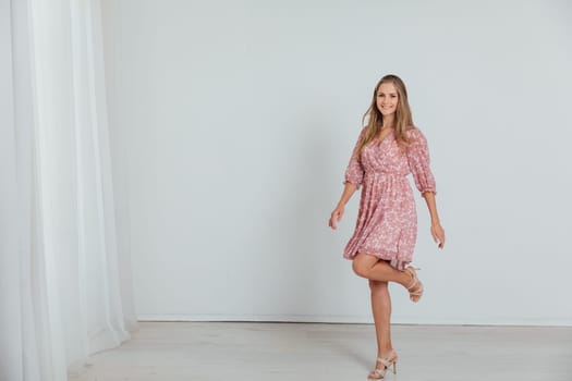 blonde woman in a pink floral dress poses in a bright room