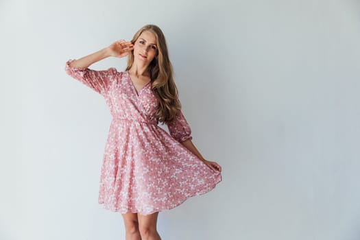 blonde woman in a pink floral dress poses in a bright room