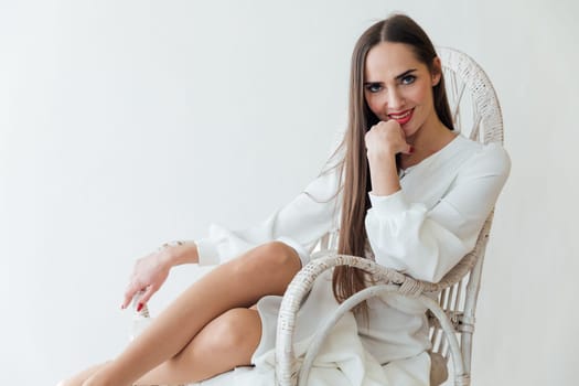 brunette in white dress sits comfortably in chair in a bright room