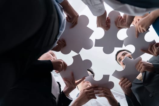 Below view of diverse corporate officer workers collaborate in office connecting puzzle pieces as partnership and teamwork concept. Unity and synergy in business idea by merging jigsaw puzzle. Concord