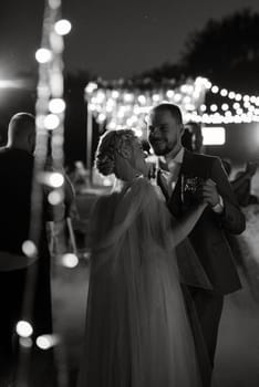 the first wedding dance of the bride and groom in the glade of the country club in the light of sunset and warm garlands