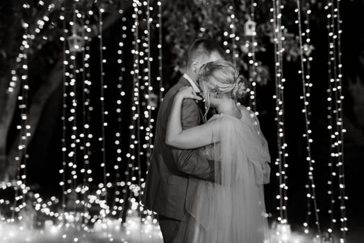 the first wedding dance of the bride and groom in the glade of the country club in the light of sunset and warm garlands