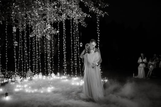 the first wedding dance of the bride and groom in the glade of the country club in the light of sunset and warm garlands