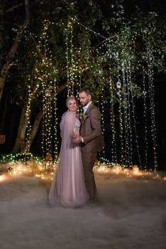 the first wedding dance of the bride and groom in the glade of the country club in the light of sunset and warm garlands