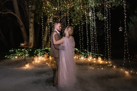 the first wedding dance of the bride and groom in the glade of the country club in the light of sunset and warm garlands