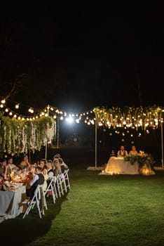 evening wedding family dinner in the forest with light bulbs and candles