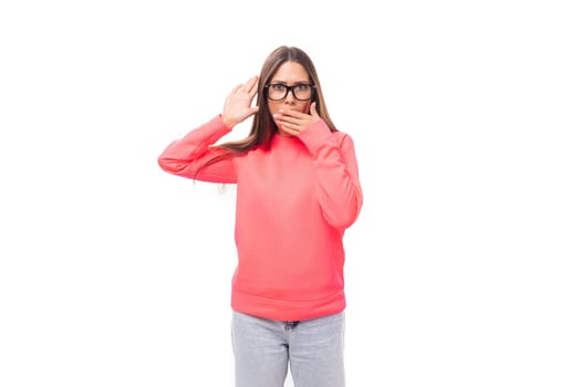 young caucasian model woman with light makeup and dark straight hair dressed in a pink sweater and jeans on a white background with copy space.