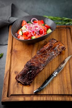 well-done steak with tomato and cucumber salad on a wooden tray