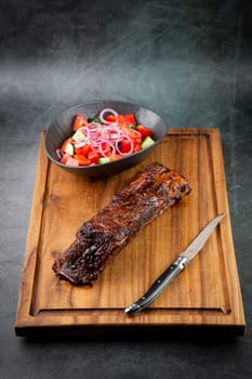 well-done steak with tomato and cucumber salad on a wooden tray