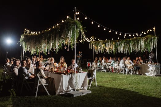 evening wedding family dinner in the forest with light bulbs and candles