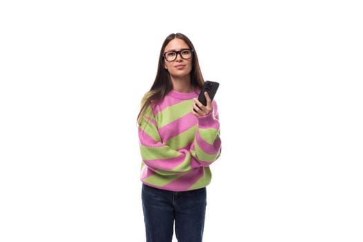 young cheerful charming caucasian woman with straight black hair dressed in a stylish autumn striped sweater holds a smartphone in her hand. mobile phone user concept.