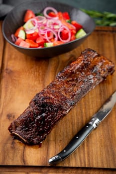 well-done steak with tomato and cucumber salad on a wooden tray