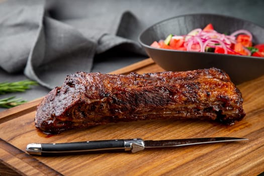 well-done steak with tomato and cucumber salad on a wooden tray