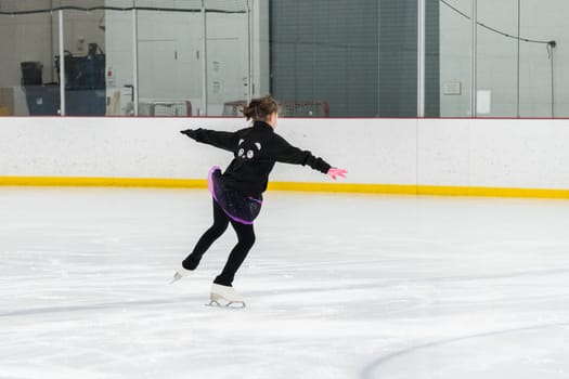 Young girl perfecting her figure skating routine while wearing her competition dress at an indoor ice rink.