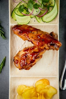 European dish. Chicken in sauce, with fried potatoes and cucumber salad, herbs and onions. dark background