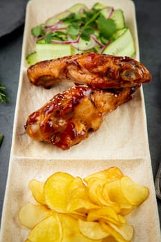 European dish. Chicken in sauce, with fried potatoes and cucumber salad, herbs and onions. dark background