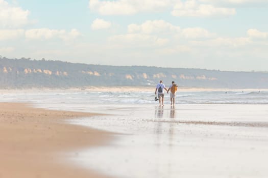 A couple of men holding his hands and walking along a beach next to the ocean - telephoto