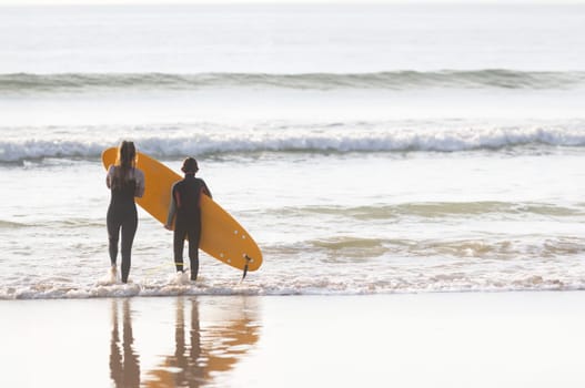 Teen boy and his mother standing in the water with surfboards