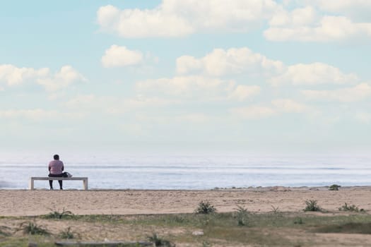 Lonely black woman sitting on a bench on the beach