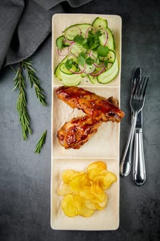 European dish. Chicken in sauce, with fried potatoes and cucumber salad, herbs and onions. dark background