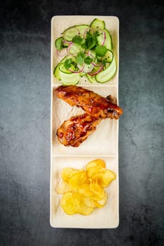 European dish. Chicken in sauce, with fried potatoes and cucumber salad, herbs and onions. dark background