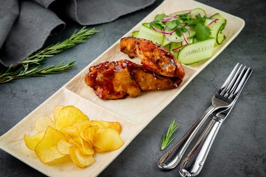 European dish. Chicken in sauce, with fried potatoes and cucumber salad, herbs and onions. dark background