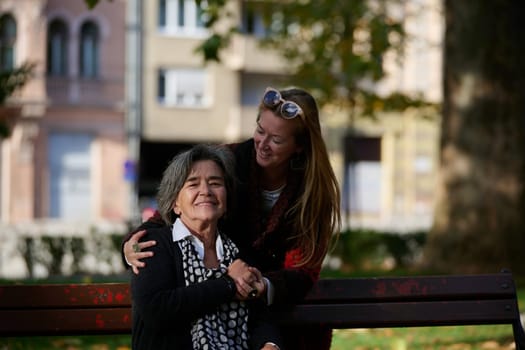 Elderly old cute woman with Alzheimer's very happy and smiling when eldest daughter hugs and takes care of her in park in autumn. Theme aging and parenting, family relationships and social care.