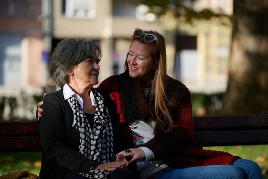 Elderly old cute woman with Alzheimer's very happy and smiling when eldest daughter hugs and takes care of her in park in autumn. Theme aging and parenting, family relationships and social care.