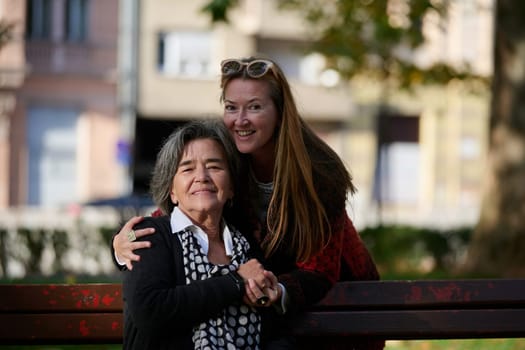 Elderly old cute woman with Alzheimer's very happy and smiling when eldest daughter hugs and takes care of her in park in autumn. Theme aging and parenting, family relationships and social care.