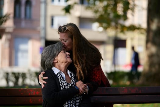 Elderly old cute woman with Alzheimer's very happy and smiling when eldest daughter hugs and takes care of her in park in autumn. Theme aging and parenting, family relationships and social care.