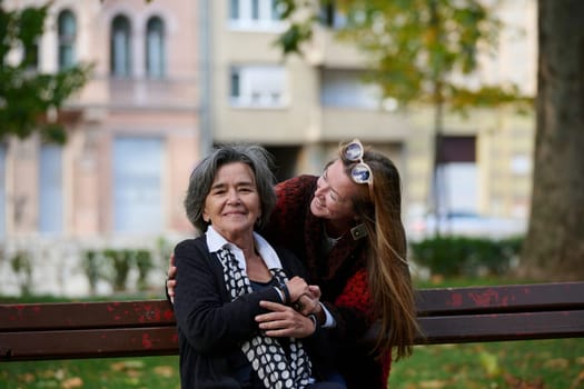 Elderly old cute woman with Alzheimer's very happy and smiling when eldest daughter hugs and takes care of her in park in autumn. Theme aging and parenting, family relationships and social care.