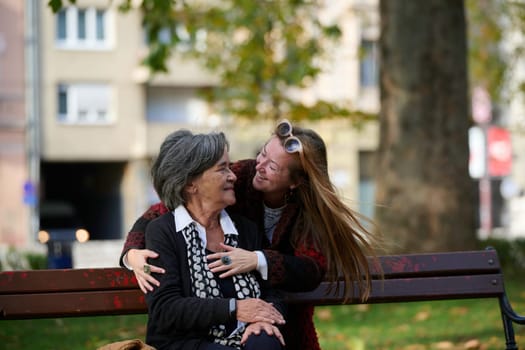 Elderly old cute woman with Alzheimer's very happy and smiling when eldest daughter hugs and takes care of her in park in autumn. Theme aging and parenting, family relationships and social care.