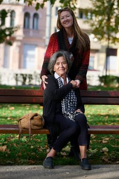 Elderly old cute woman with Alzheimer's very happy and smiling when eldest daughter hugs and takes care of her in park in autumn. Theme aging and parenting, family relationships and social care.